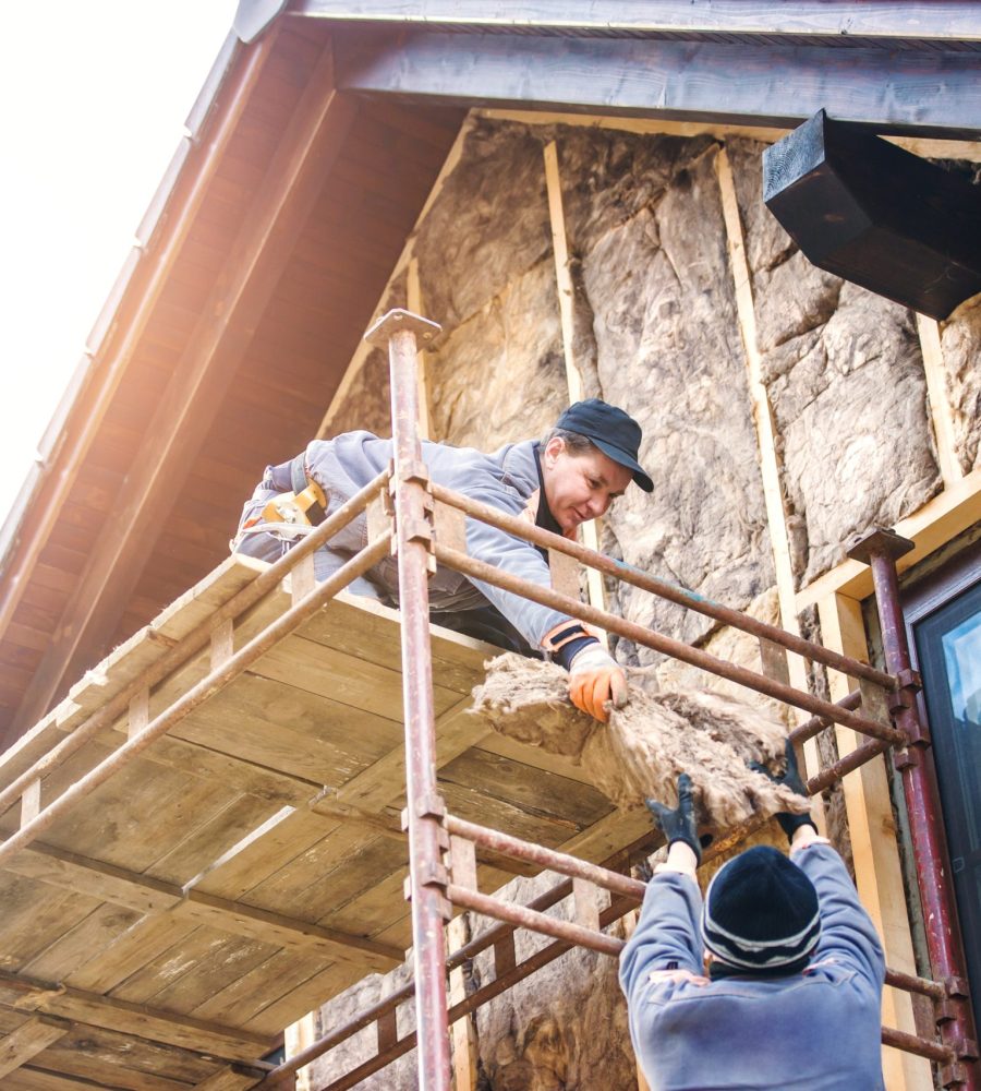 Construction workers standing on scaffold thermally insulating house facade with glass wool.